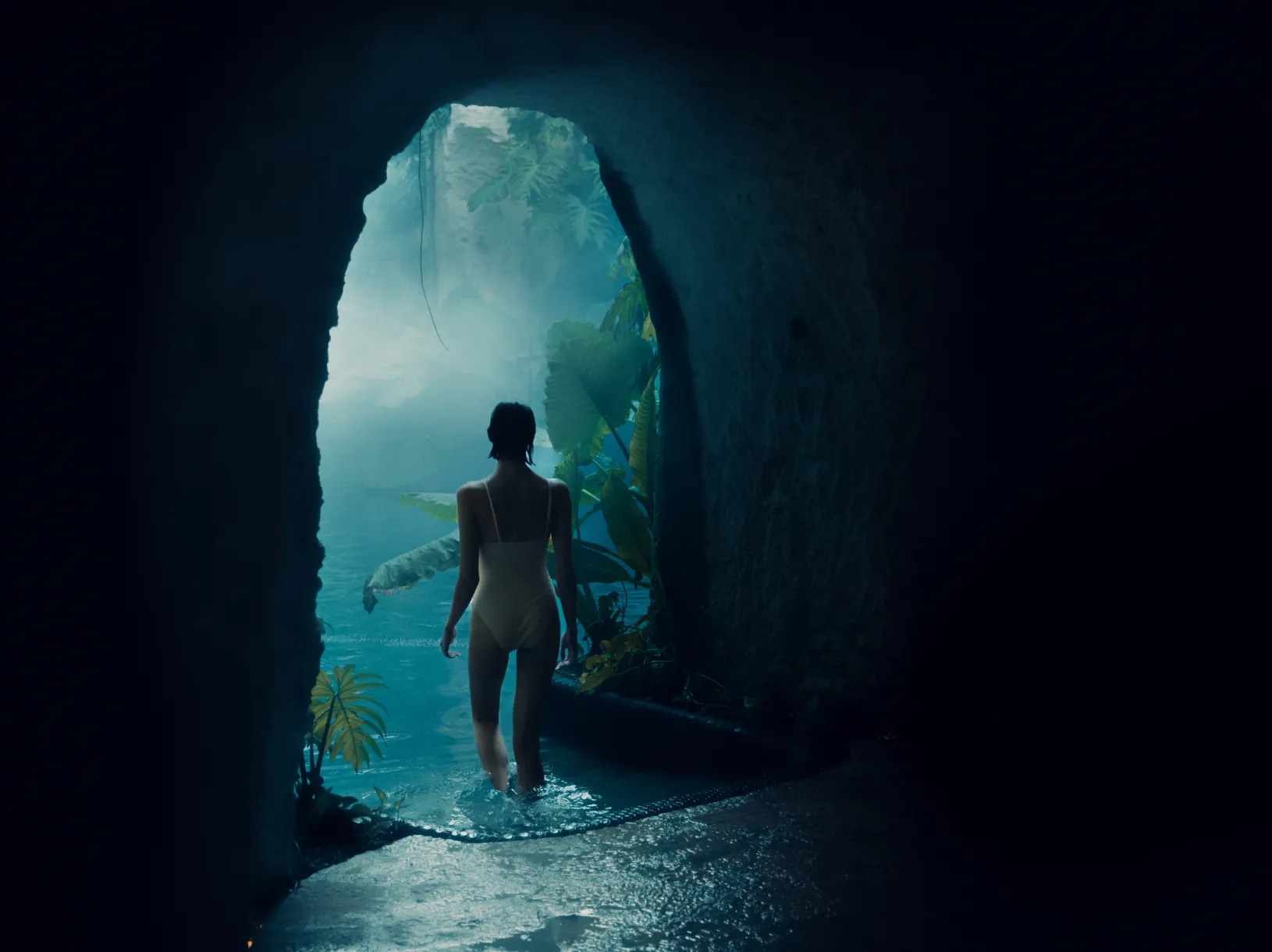 A woman in a swimsuit walking out of a dark, wet cave.