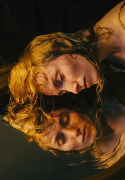 A woman leaning over with eye closed and a reflection of her.