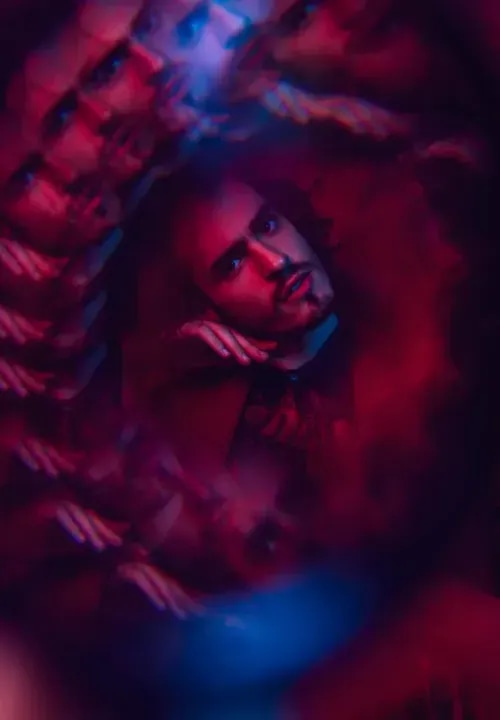 A bearded man posting with a swirl with kaleidoscope-like reflections wrapped all around him.