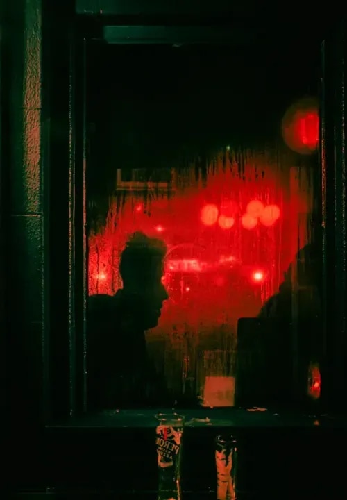 A view from the outside of a bar window a silhouette of a person and a reflection of red stoplights