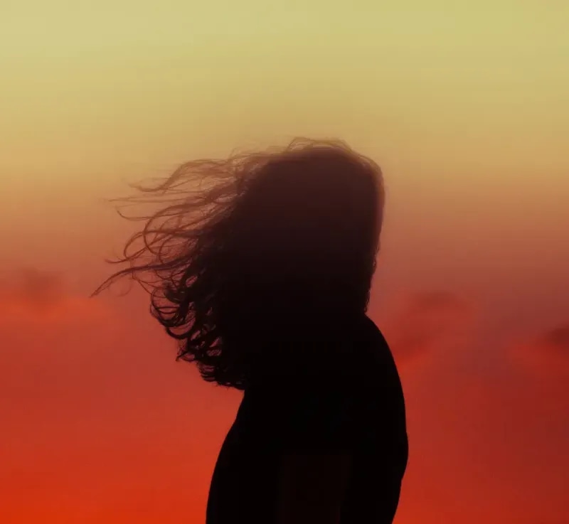 A silhouetted person standing in front of a golden sky with their hair flowing in the wind