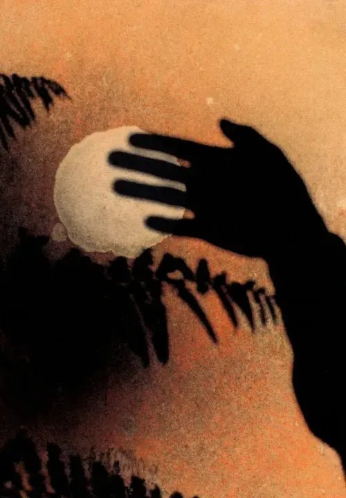A silhouetted hand held up in front of the moon in the sky.