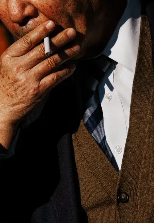 A elder man in a suit smoking a cigarette.