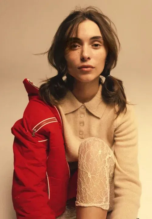 A young woman posing with a bright, red jacket hanging on her shoulder.
