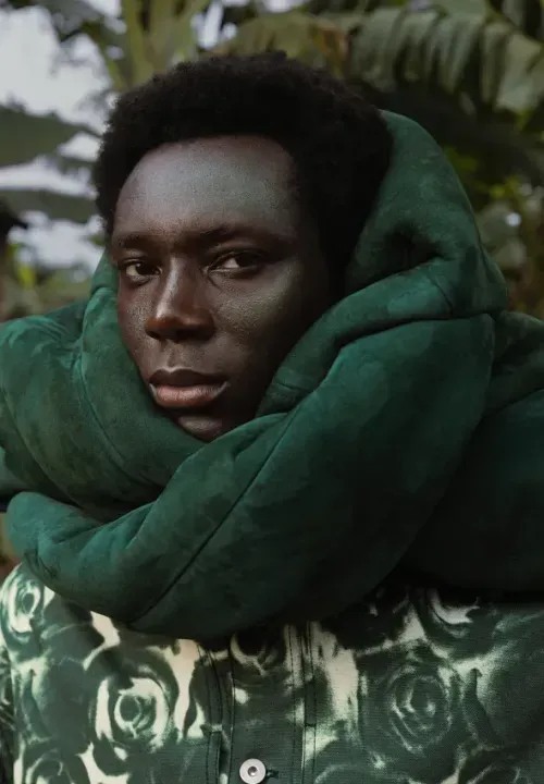 A person posing in a green floral shirt and green, puffy scarf.
